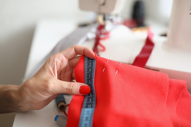 Female hands hold fabric and a measuring tape near the sewing machine the seamstress designer