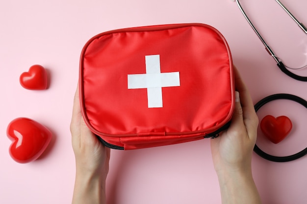 Female hands hold first aid medical kit on pink