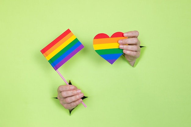 女性の手は、緑の背景に虹の色で旗とハートを保持しています。 LGBTの概念。広告のための場所。