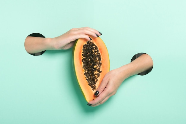 Фото Женские руки держат свежую папайю через отверстие на фоне неоновой мяты