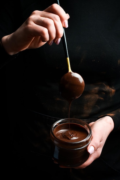 Женские руки держат стеклянную банку с расплавленным шоколадом Кухонная утварь на черном фоне