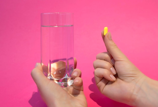 Female hands hold a glass of water and a pill on a pink background Health and medicine