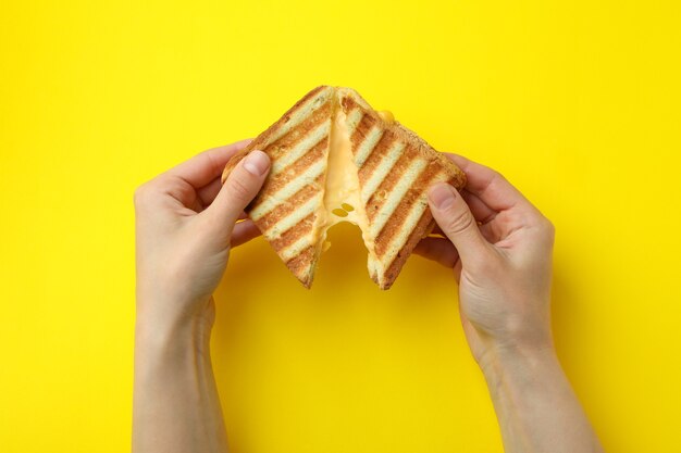 여성의 손을 잡고 노란색 배경에 치즈와 구운 된 샌드위치