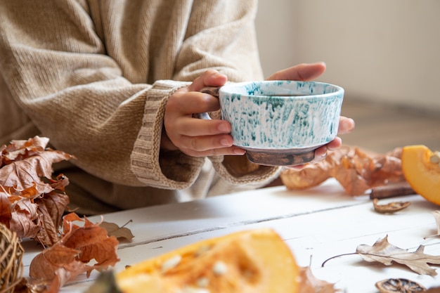 Female hands hold a handmade ceramic cup with a hot drink on a blurred background.