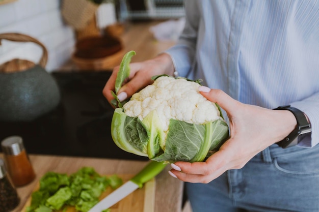 Le mani femminili tengono una testa di cibo vegano di cavolfiore