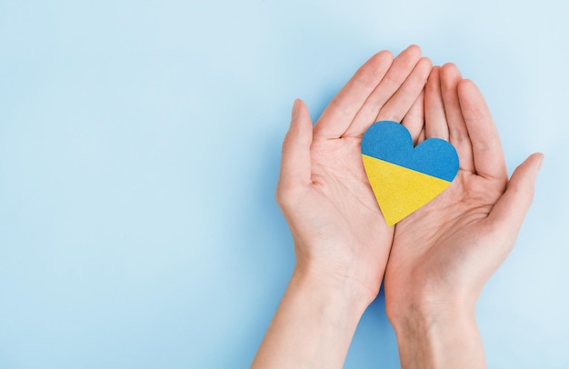 Female hands hold a heart painted in the colors of the\
ukrainian flag