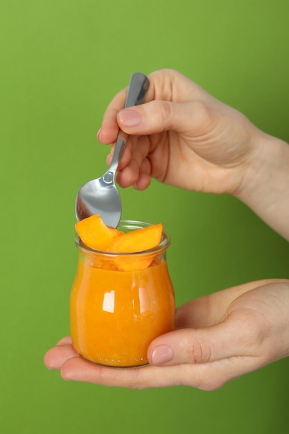Female hands hold jar of pumpkin jam and spoon on green background