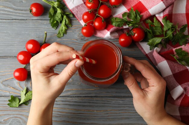 Female hands hold jar with tomato juice on wooden board with tomatoes