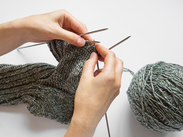 female hands hold knitting needles and yarn and knit a sock or scarf