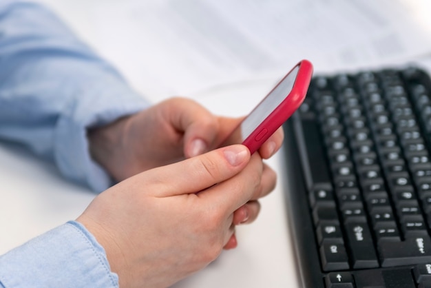 Female hands hold mobile phone against the background of computer keyboard. SMM manager. Promotion of social networks.