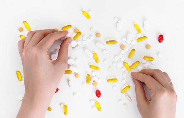 Female hands hold multi-colored pills on a white surface. Top view. Health concept.