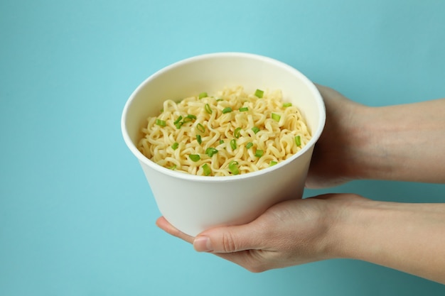 Female hands hold paper bowl with cooked noodles on blue