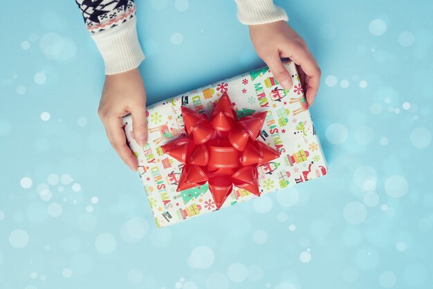 female hands hold a paper closed box with red bow on a blue 