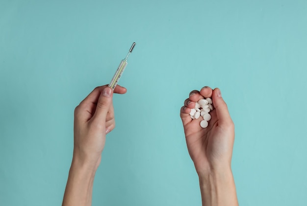 Female hands hold pills and thermometer on blue paper