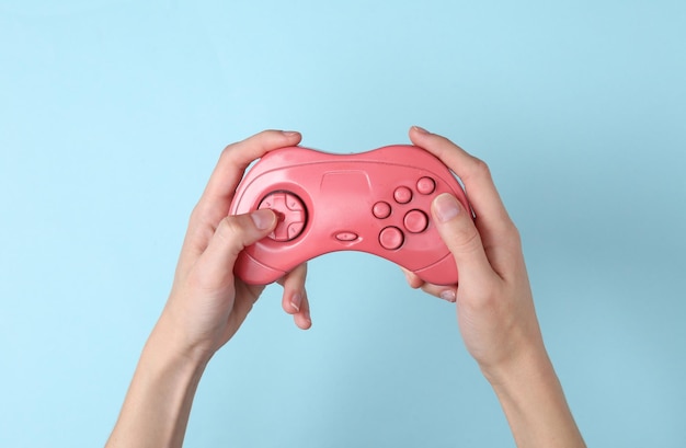 Female hands hold a pink retro gempad on blue background Gaming concept