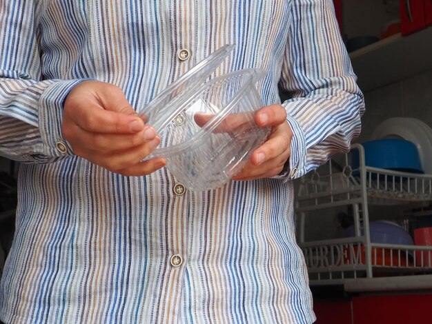 Female hands hold a plastic container or packaging Kitchen utensils A woman in a white striped shirt stands in the kitchen and shows a disposable plastic box with a lid Hygiene and recycling theme