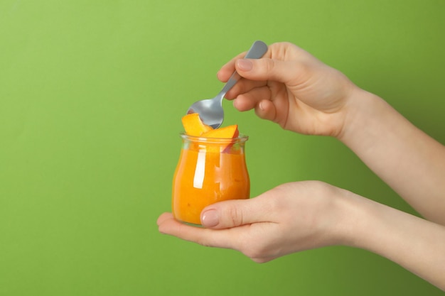 Female hands hold pumpkin jam on green background