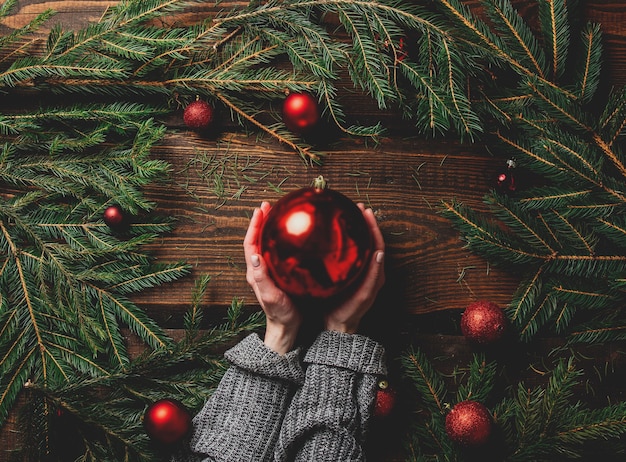 Female hands hold red bauble next to Christmas decoration