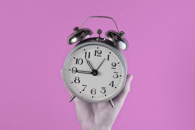 Female hands hold retro alarm clock on pink