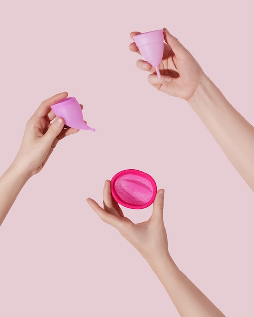 Female hands hold reusable menstrual disc and cups on pink background