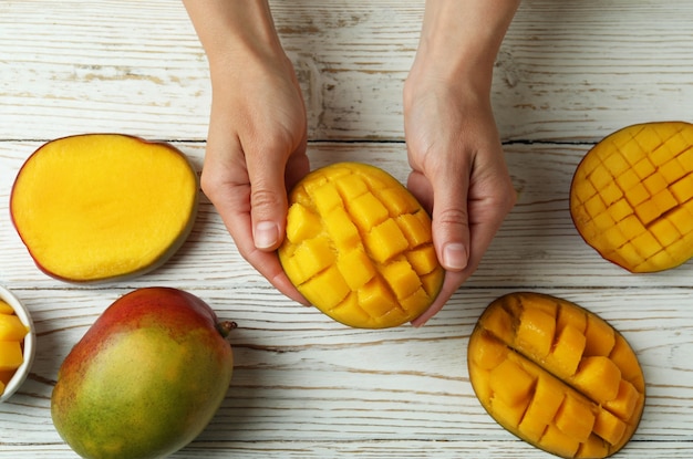 Female hands hold ripe mango fruit on wooden table