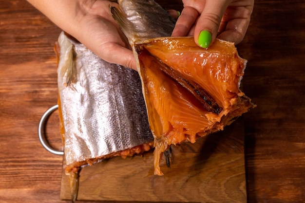 Female hands hold a salmon carcass and unfold the cut against the background of a cutting board