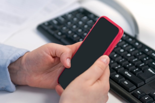 Female hands hold smart phone against the background of computer keyboard. SMM manager. Promotion of social networks.