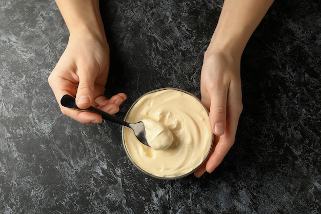 Female hands hold spoon and bowl with mayonnaise on black smokey background