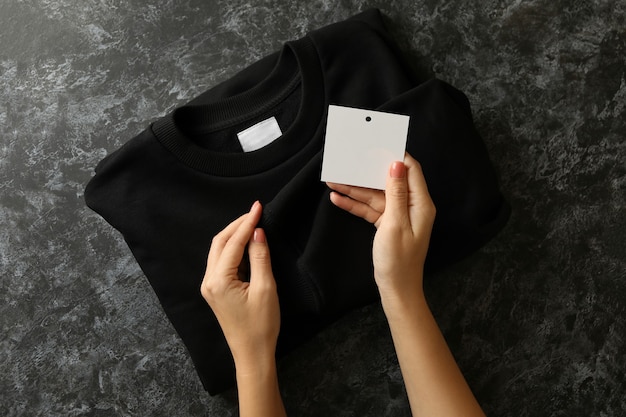 Female hands hold sweatshirt and tag on black table