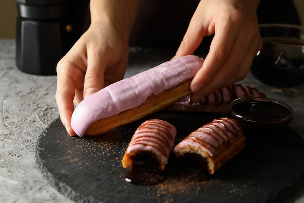 Female hands hold tasty eclair on gray table with eclairs, close up