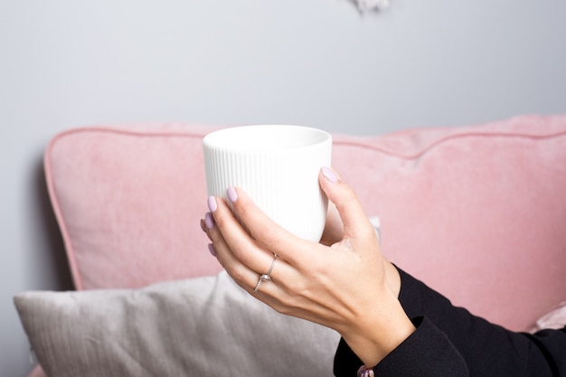 Le mani femminili tengono il tè in tazza di ceramica bianca in un interno rosa