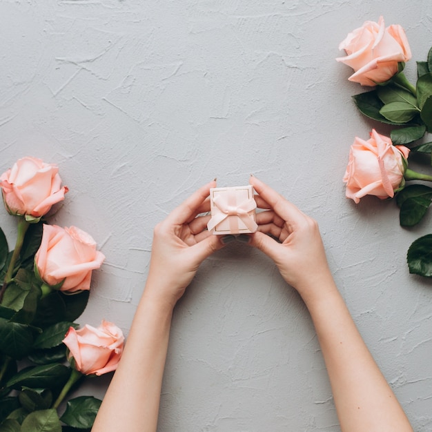 Female hands hold a wedding ring on a gray background.