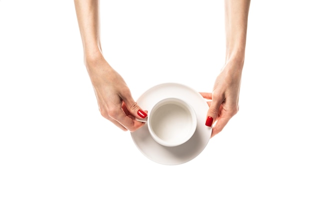 Female hands hold a white ceramic cup with a saucer on white background Female hands with fresh red manicure Isolated on white background