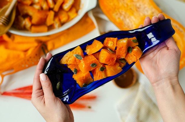 Female hands holding baked pumpkin on a hand crafted blue serving plate on white background.