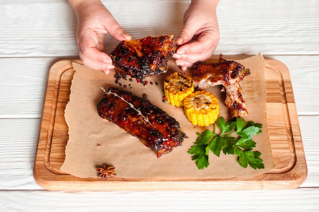 Female hands holding barbecue meat above wooden board with meat and corn