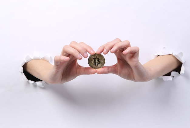 Female hands holding bitcoin through torn hole white paper Concept art