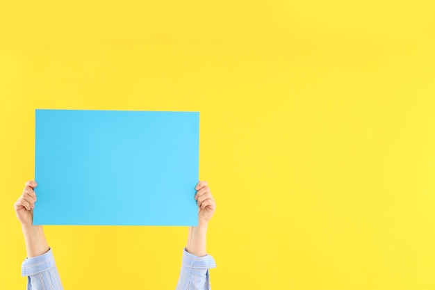 Female hands holding blank banner on yellow background