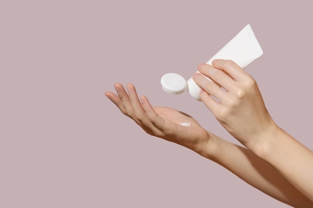 Mani femminili che tengono un tubo cosmetico in plastica bianca vuota su sfondo rosa mockup