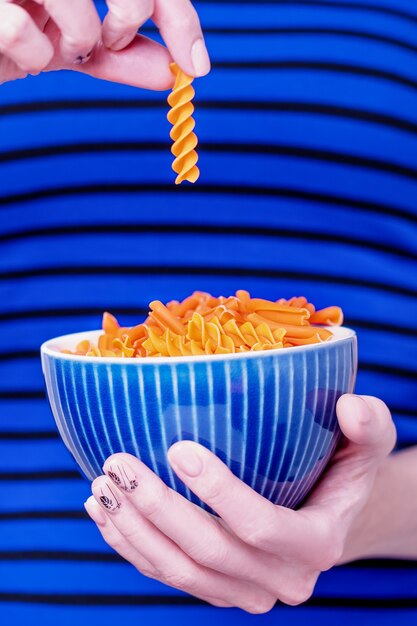 Foto mani femminili che tengono ciotola blu con pasta di fusilli di lenticchie arancioni sul blu