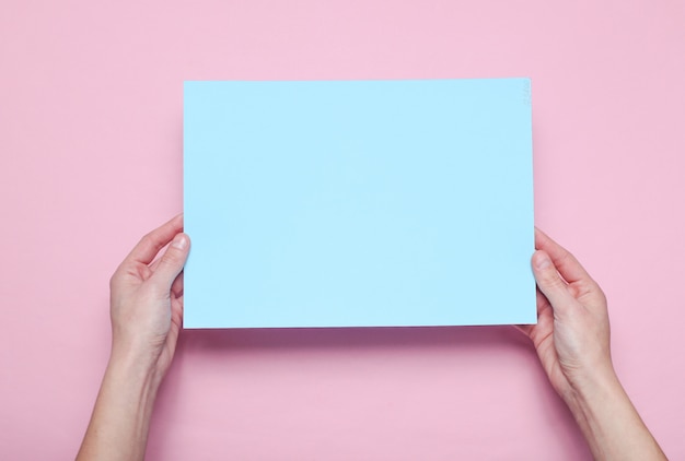 Female hands holding blue paper sheet on pink