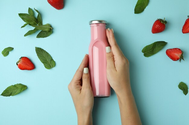 Female hands holding bottle of strawberry milkshake on blue background