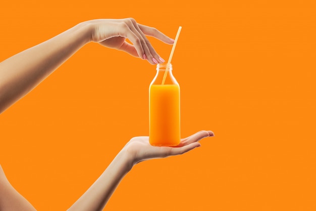 Female hands holding bottle with straw of fresh detox orange juice