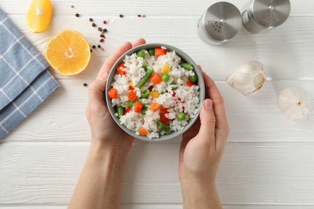 Female hands holding bowl of delicious rice on wood surface