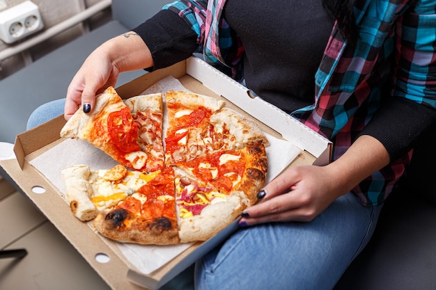 female hands, holding a box with different types of pizzas, eating, biting and tearing, light and da