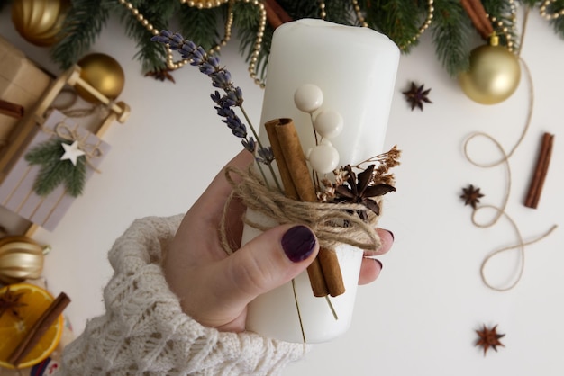 Female hands holding a Christmas candle on a white background in the middle of Christmas decor