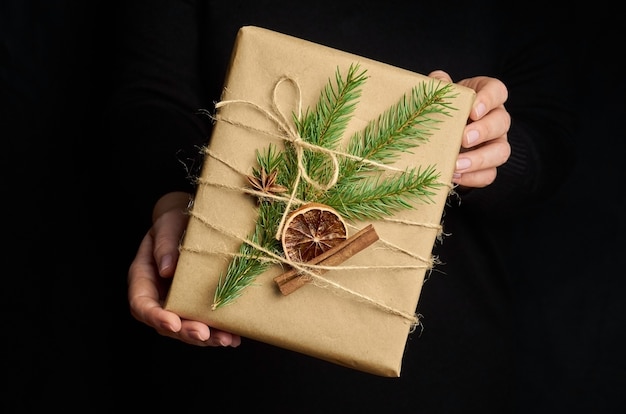 Female hands holding Christmas gift box over black