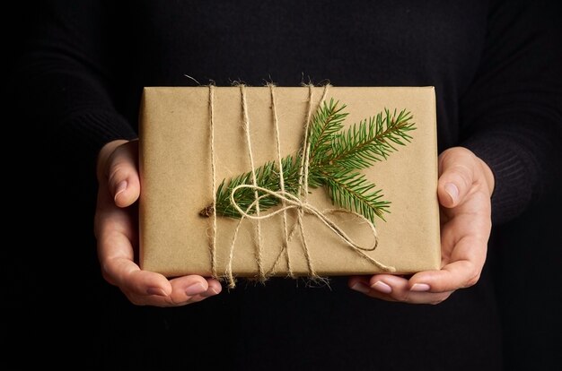 Female hands holding Christmas gift box over black