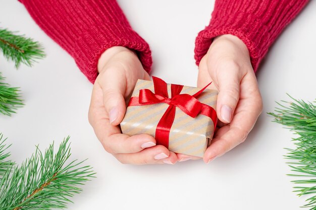 Female hands holding christmas gift box with red bow over white background