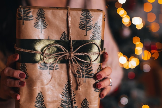 Female hands holding a Christmas gift wrapped in festive beige paper Festive winter holidays