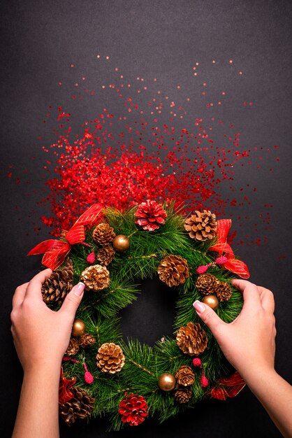 Female hands holding christmas wreath over black  with red glitter and copyspace